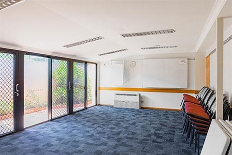 Room with white walls, blue carpet and red chairs stacked against a wall