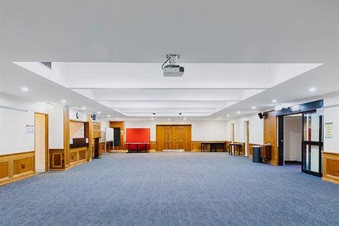 Big room with white walls, blue carpet and doors on either side of the room