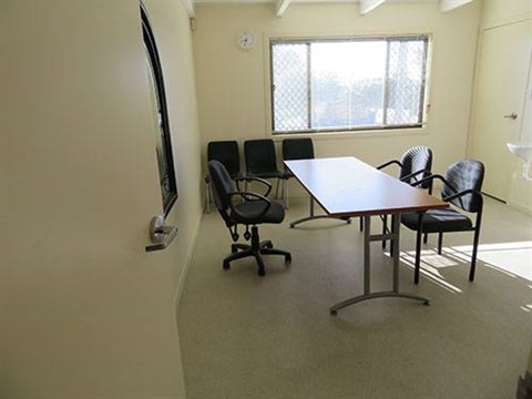 Long desk in centre of room surrounded by black chairs