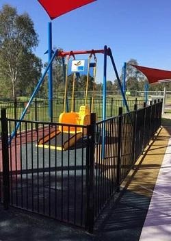 A yellow swing in the park that is fenced and a wheelchair can access to enjoy a swing.