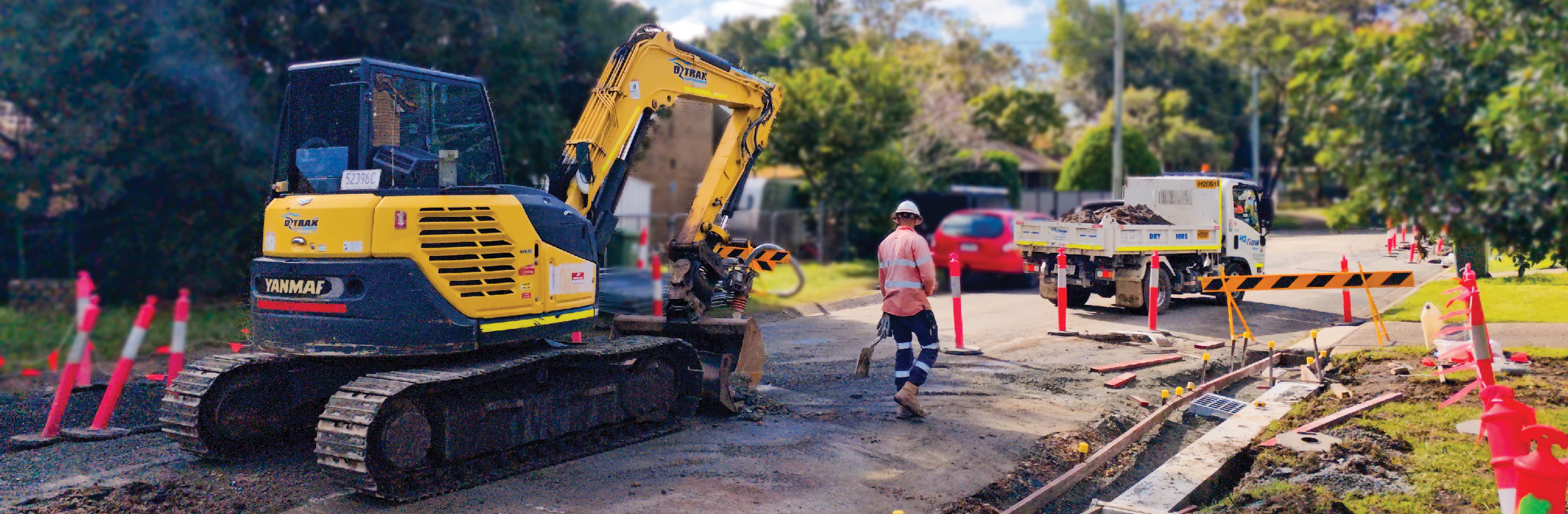 Roadworks underway on a suburban street, with an excavator and construction worker in high-visibility gear