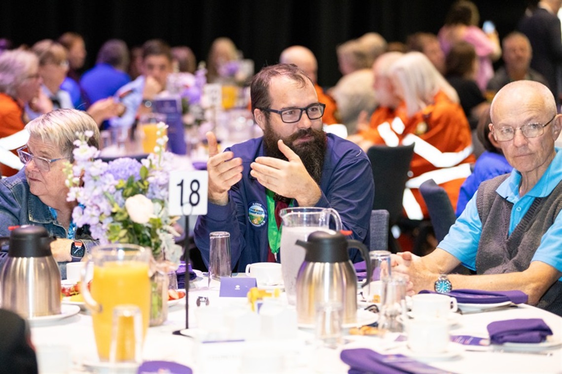 A group of volunteers sitting around a round table taking while attending the volunteers breakfast