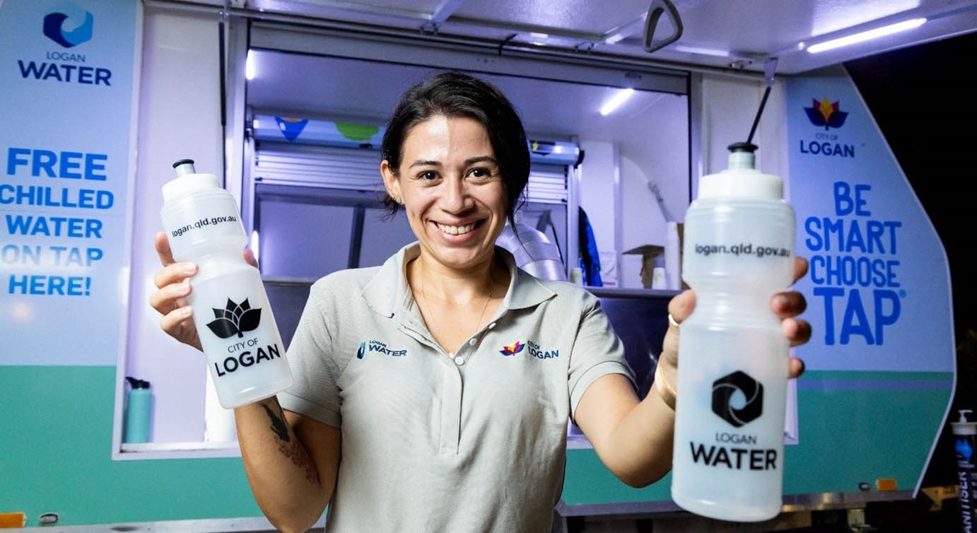 Woman holds up empty Logan Water water bottles while standing in front of Water Wagon