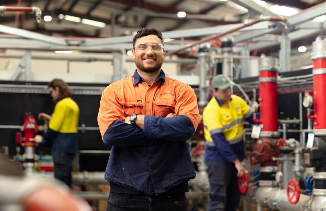 Man dressed in high visibility clothing stands arms folded and smiling in a factory environment