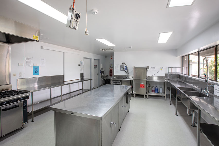 Large commercial kitchen with multiple stainless steel food preparation areas, sinks and ovens.
