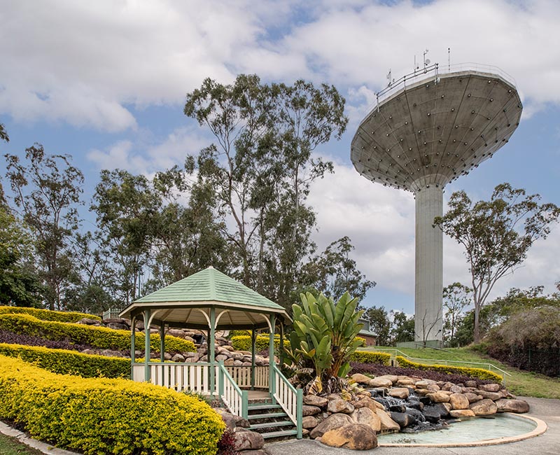 Rotunda and waterfall in garden area with water tower in distance behind the area