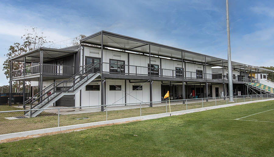 White two story building sitting at the edge of a sports field