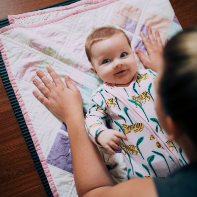 A baby lying on a blanket with a mother leaning over them