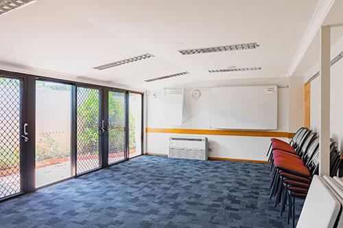 Room with white walls, blue carpet and red chairs stacked against a wall.