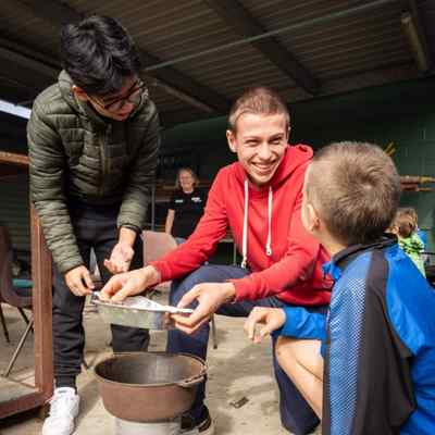 Kids sit on and outdoor bench with a cooking pot in front of them