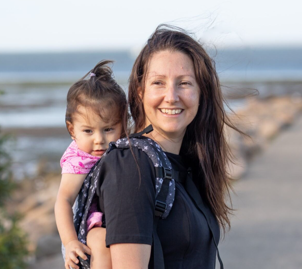 A lady walking along a path near the ocean with her baby in a carrier on her back