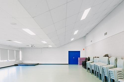 Large white room with sloped roof. Chairs and mats piled along the wall