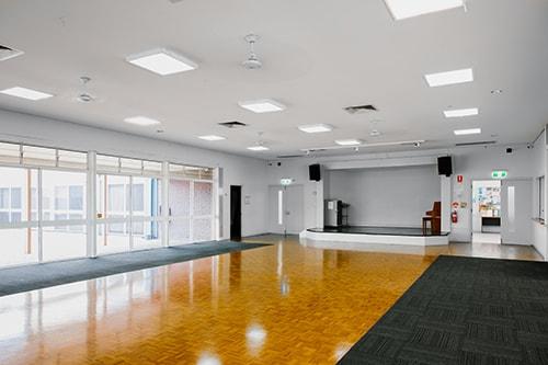 Large room with a small stage. Lots of light due to numerous windows and doors on one side of the room.