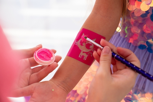 Child with a pink star stencil on their arm that is being painted on