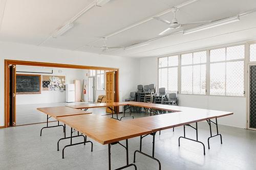 Large white room with 6 tables in the middle of the room and chairs stacked to the side.