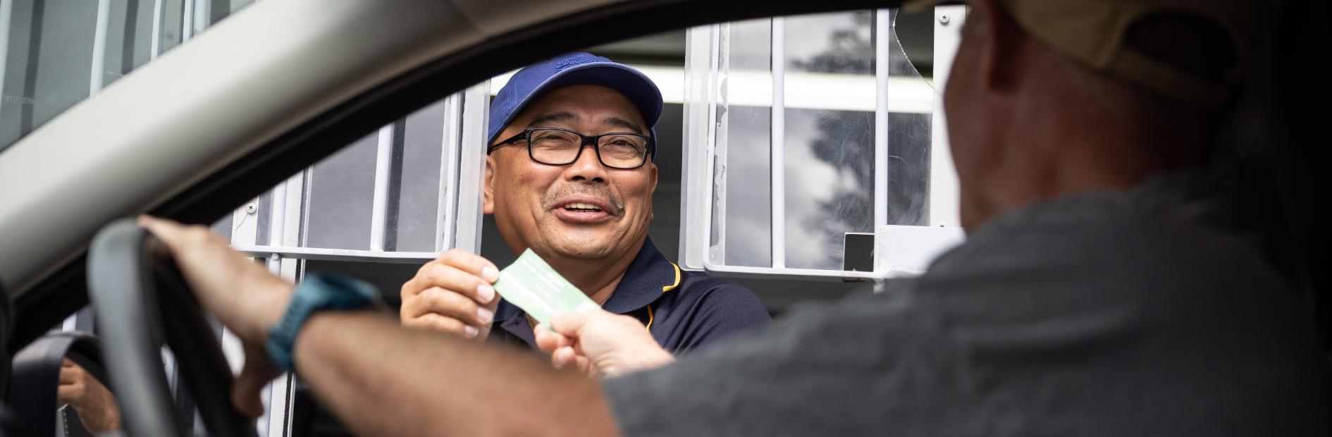 Man in council uniform in drive through window hands a customer in their car a piece of paper