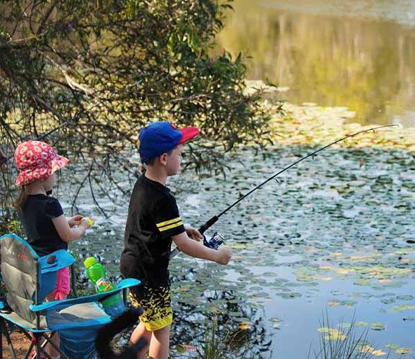 Children standing on edge of water with fishing rods