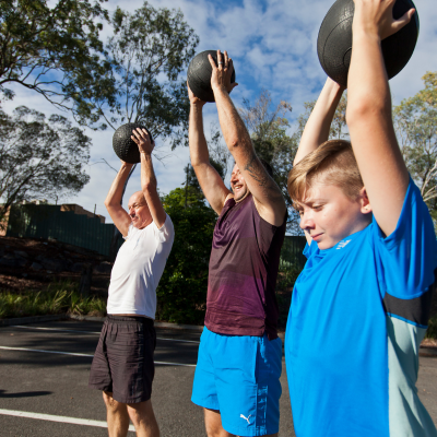 Three men lined up holding a weighted exercise ball above their heads