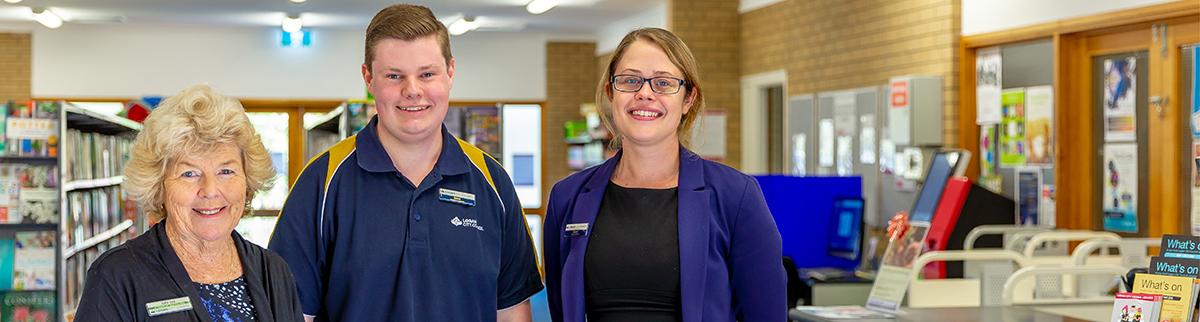 two women and a man standing and smiling inside a library