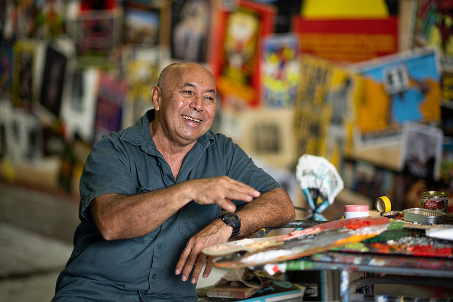 Artist Gordon Hookey smiling while sitting among paint palettes and artworks