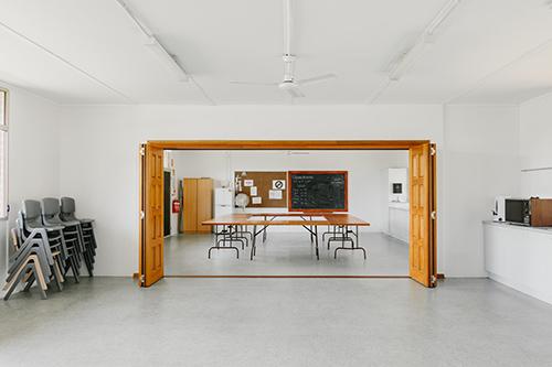 Large room with doors leading to another room with tables and chairs in