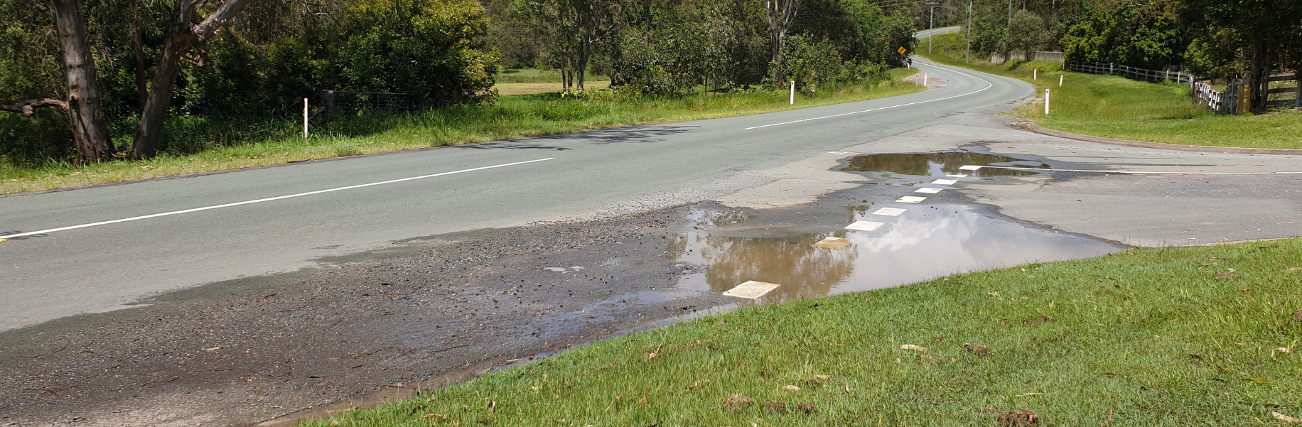 Current intersection of Spring Mountain Drive and Raglan Road. Shows water partially covering road that isn't well maintained. 