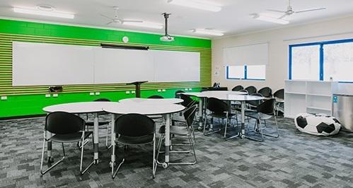 Large white room with a green feature wall. Several whiteboards and tables in the room and a projector on the roof.