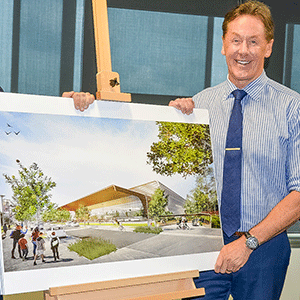 Mayor stands with artist impression of sports venue on easel