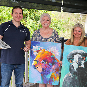 Lifestyle Chair Councillor Tony Hall previews the paint and sip sessions offered by Logan Artists Association’s Di Flack (centre) and Kristy Flynn (right) at this year’s Logan Seniors Big Day Out.