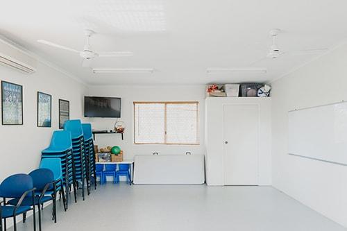 Large white room with blue chairs stacked on the left side of the room and a white board on the wall on the right side of the room.