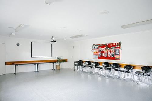 large white room with a projector and seats stacked along the wall