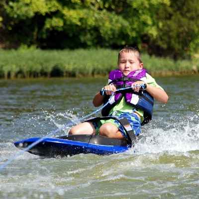 Young girl dressed in life vest hangs onto cable and is pulled along water on a kneeboard