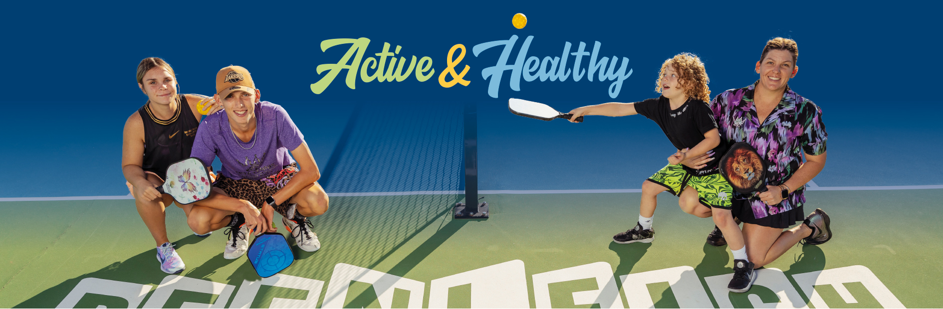 Two sets of two people smile while crouching on opposite sides of a tennis court. Logo reads: Active and Healthy
