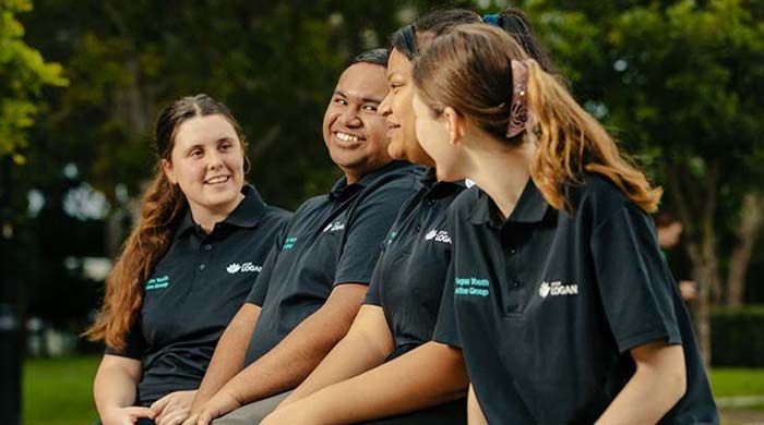 Four young people dressed in matching uniform tops sit and smile together