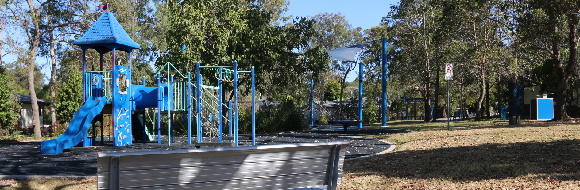 A public park bench with a blue Childrens' playground in the background.