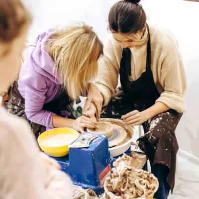 Child and woman work together to form clay on a pottery wheel