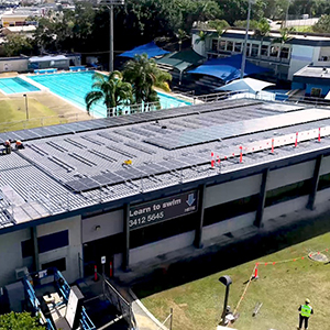 An image of workers installing solar panels on the roof of Logan North Aquatic Centre. Logan City Council is leading the way in solar initiatives on city buildings.