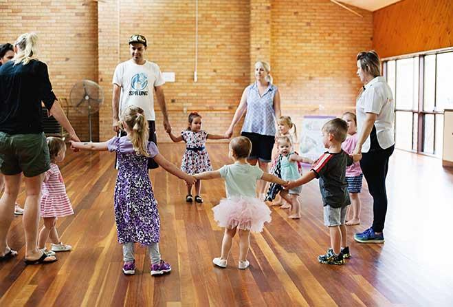 Young kids standing in a circle with adults holding hands.