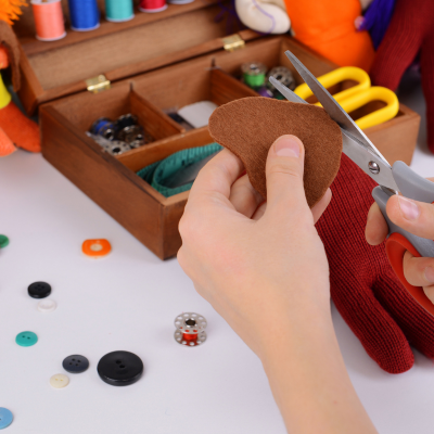 Child cutting brown paper with scissors. Assorted buttons and other craft materials are visible nearby.