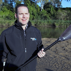 An image of Deputy Mayor Jon Raven holding a paddle on the banks of the Logan River as he urges safety while using the new kayak and canie trails