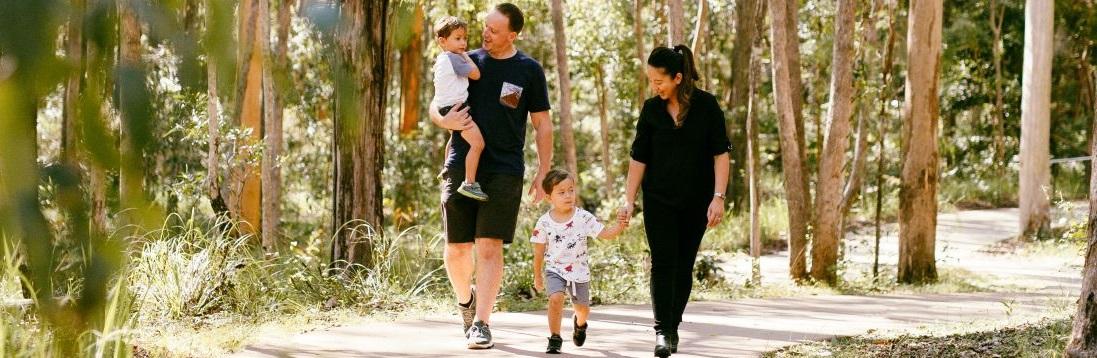 A family, mother, father and two young boys out for a walk on a winding path through the trees in a park