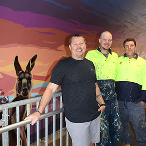 An image of Division 9 Councillor Scott Bannan (front) at the Jimboomba Safe Crossing with Logan City Council mural artists Paul Turnbull (left) and Jay Christensen inside the tunnel which features a kangaroo painting.