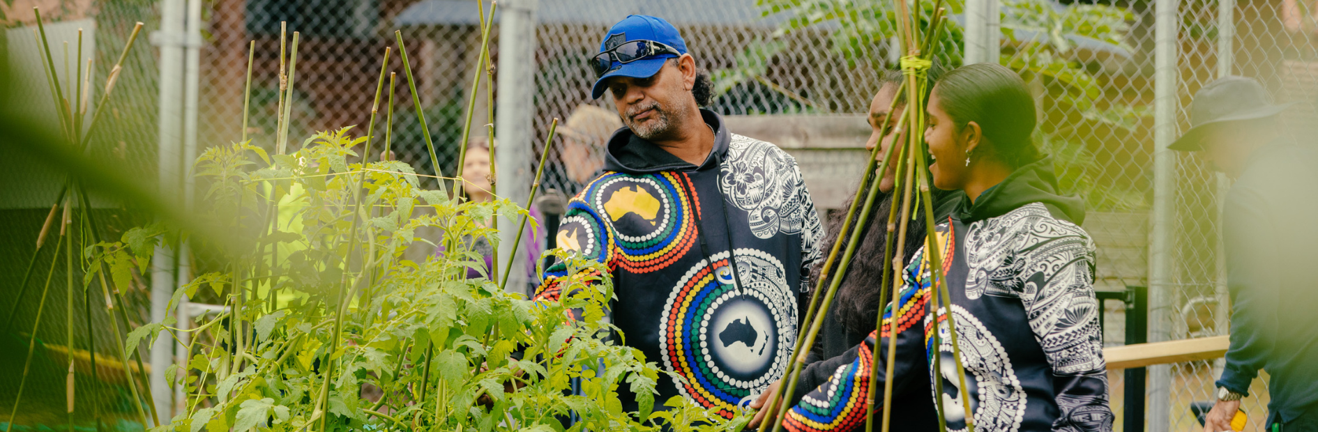 Man and two women dressed in colourful jumpers with indigenous prints on them chat and laugh in a vegetable garden