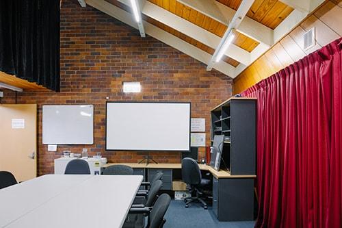 large room with brick walls and slanted roof. Red curtain on right had side and whiteboard on wall