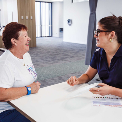 Older woman and a younger woman in Health worker uniform laugh while seated at a table together