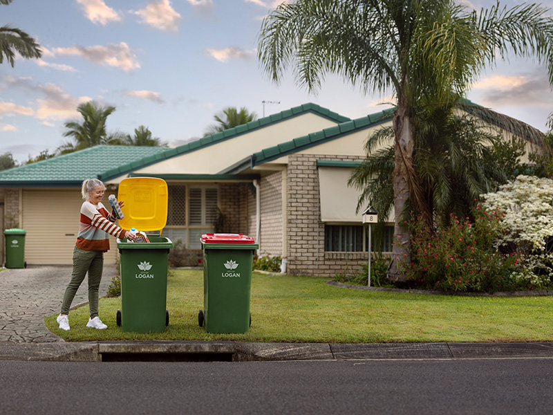 Woman placing egg carton and plastic bottle in yellow lid bin