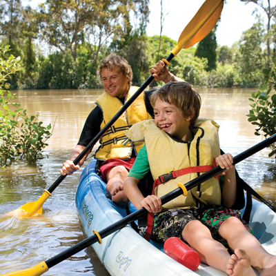 Young man and boy sitting in a kayak on a river. Each hold a double sided paddle.