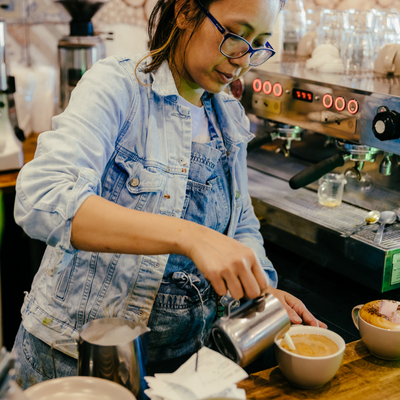 Woman in a cafe pouring hot milk into a mug to make a coffee
