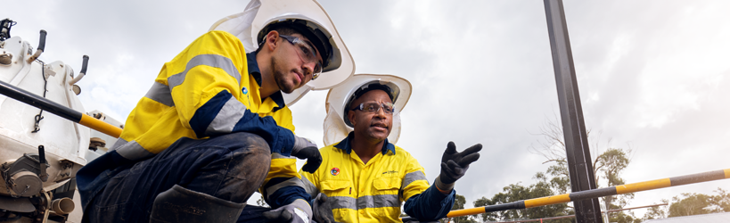 Two men dressed in high vis crouch behind a crouch and chat