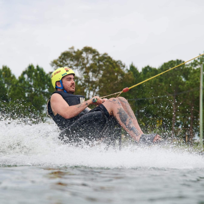 Man in sitting position wakeboards on the water